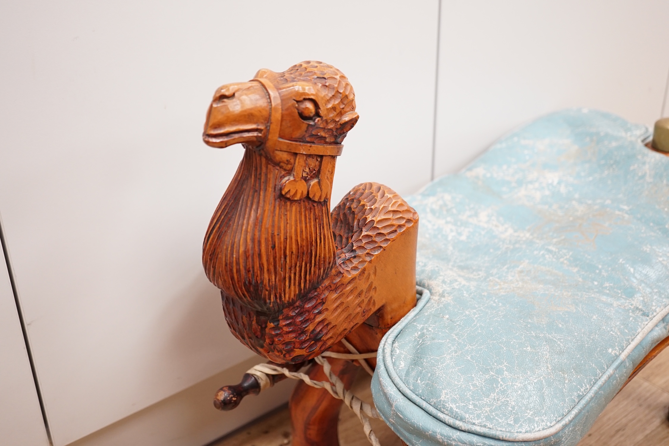 A carved wood foot stool in the form of a camel, blue stamped patterned leather cushion, 56cm high, 71cm wide. Condition - frame good, leather cushion worn